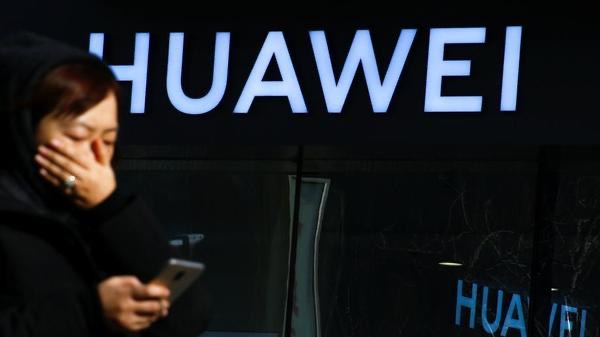 A woman using a phone in front of a Huawei sign